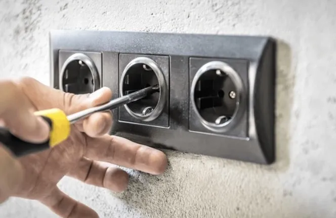 Drievoudig antracietkleurig stopcontact wordt afgemonteerd op een betonwand