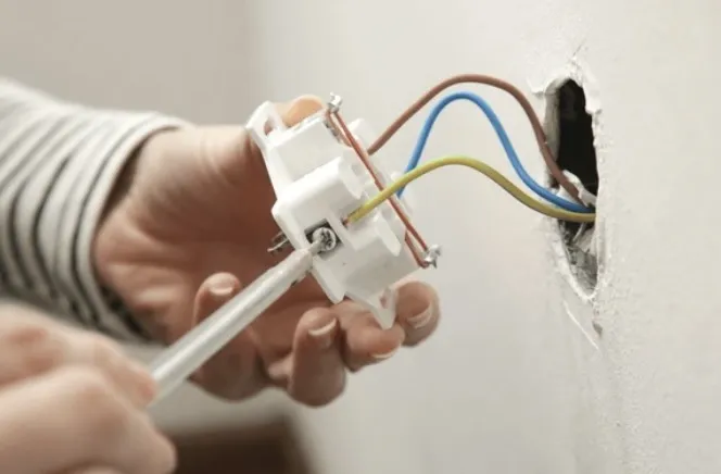 Elektricien sluit een stopcontact aan in een uitgefreesde wandopening